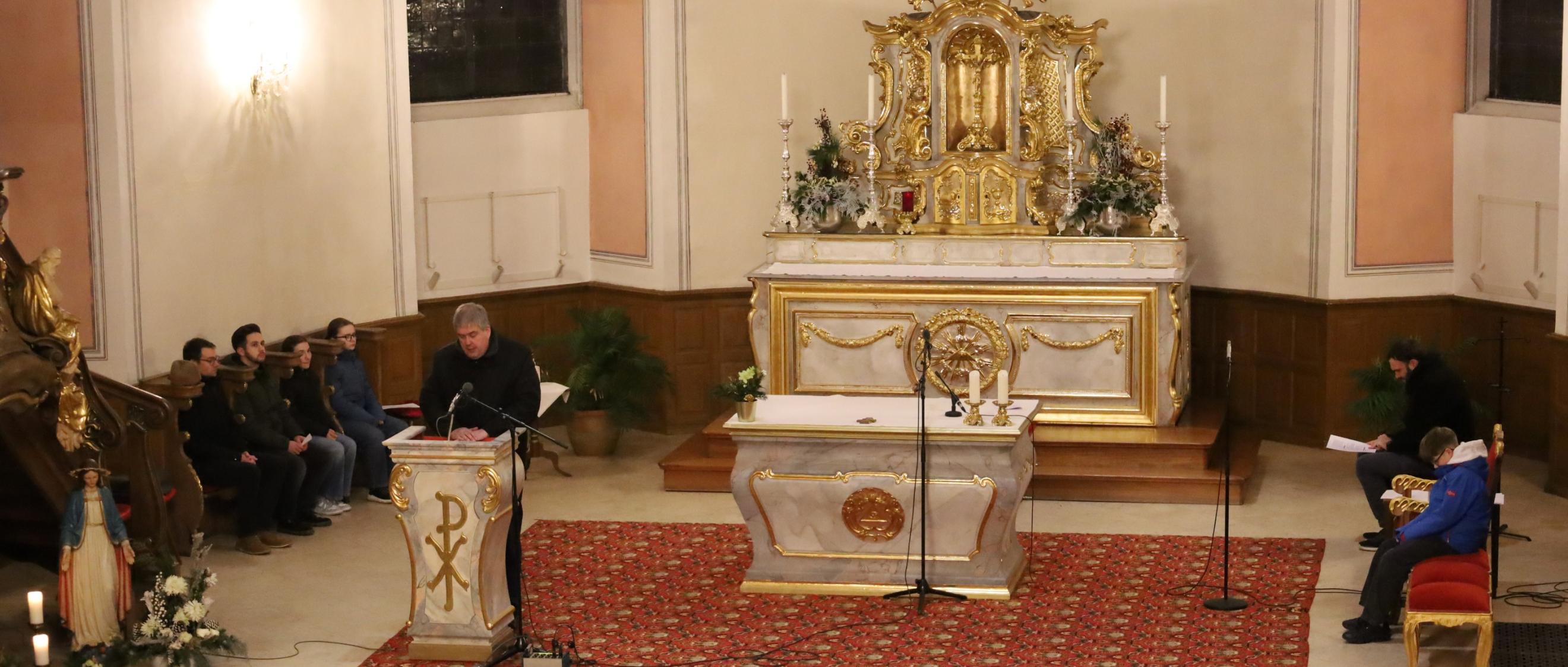 Altar von oben; ein Priester predigt; auf den Seitenbänken sitzen Personen und beten