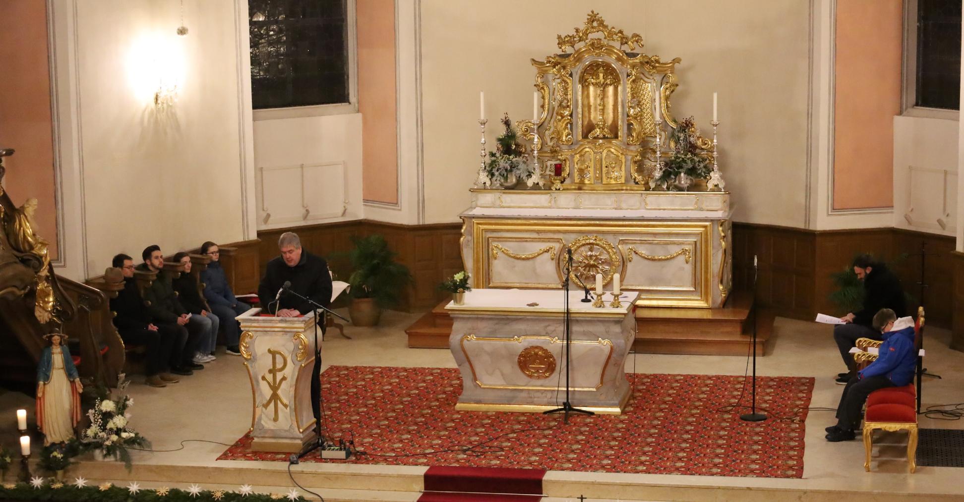 Altar von oben; ein Priester predigt; auf den Seitenbänken sitzen Personen und beten