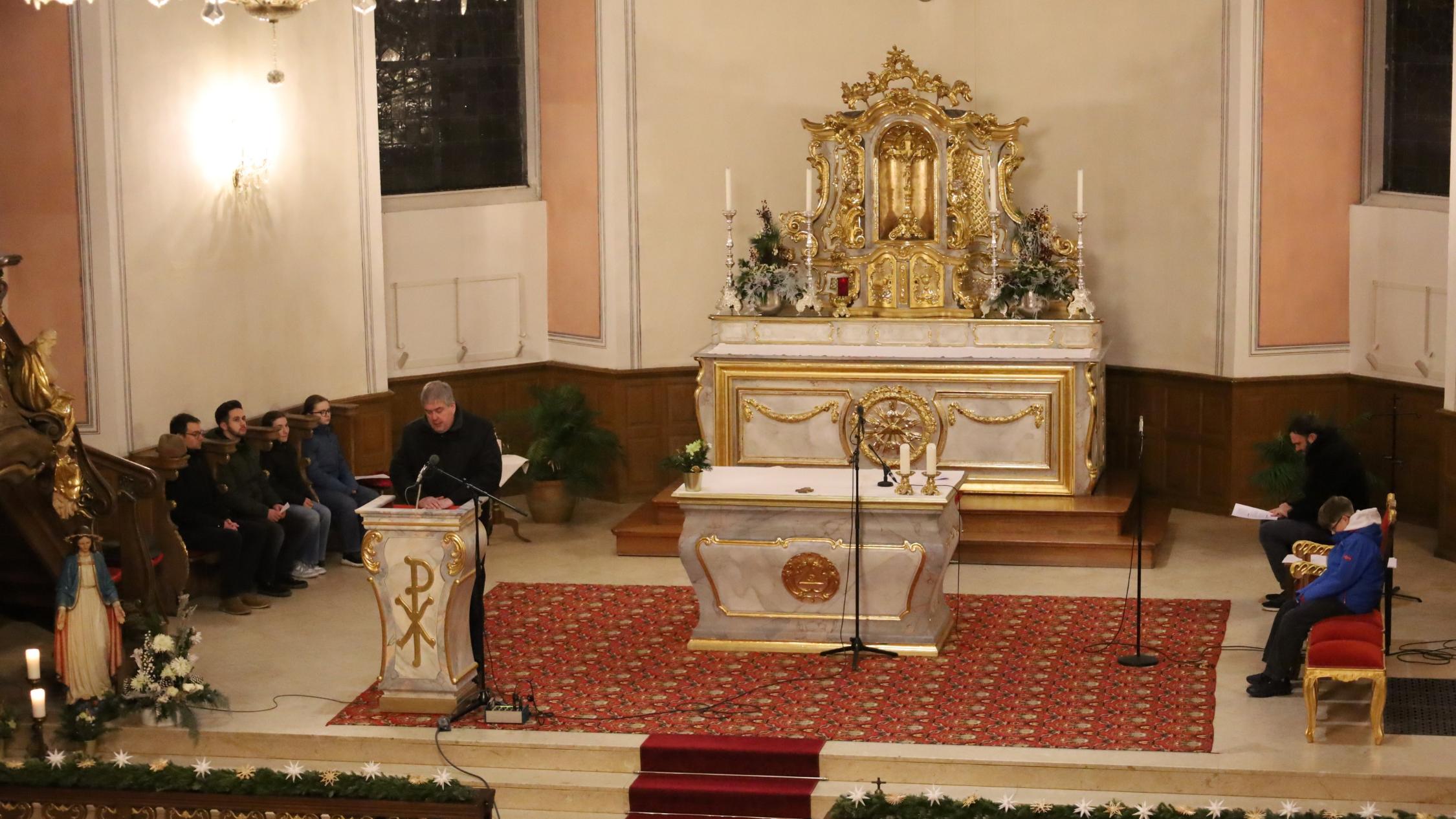 Altar von oben; ein Priester predigt; auf den Seitenbänken sitzen Personen und beten