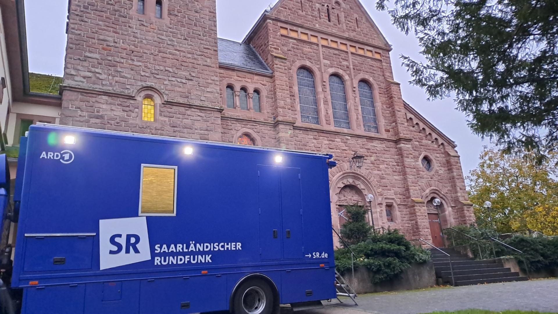 Ein blauer Ü-Wagen des SR steht vor der Kirche.