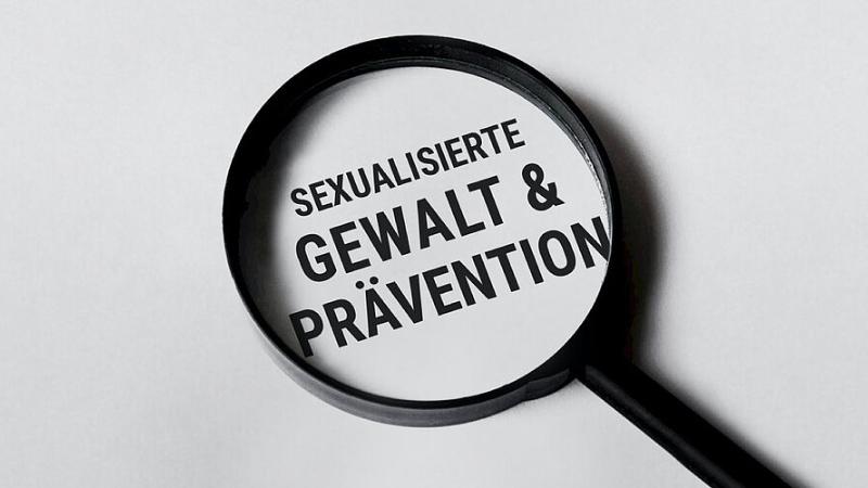 Man sieht eine Lupe mit dem Text 'Sexualisierte Gewalt & Prävention'