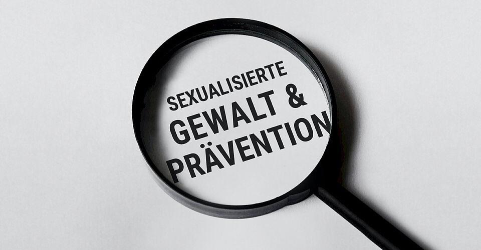 Man sieht eine Lupe mit dem Text 'Sexualisierte Gewalt & Prävention'