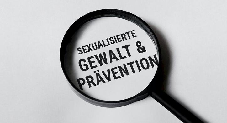Man sieht eine Lupe mit dem Text 'Sexualisierte Gewalt & Prävention'