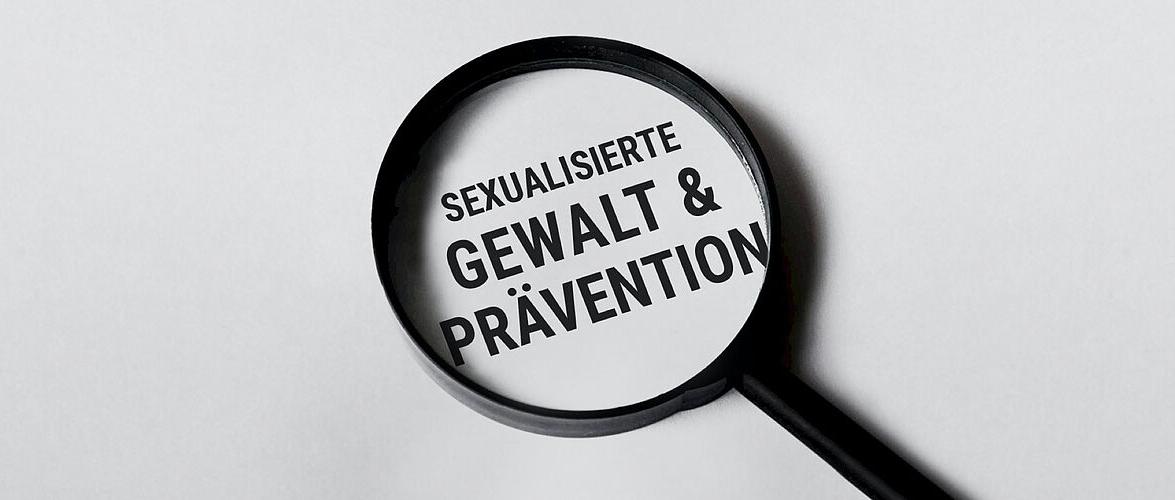 Man sieht eine Lupe mit dem Text 'Sexualisierte Gewalt & Prävention'