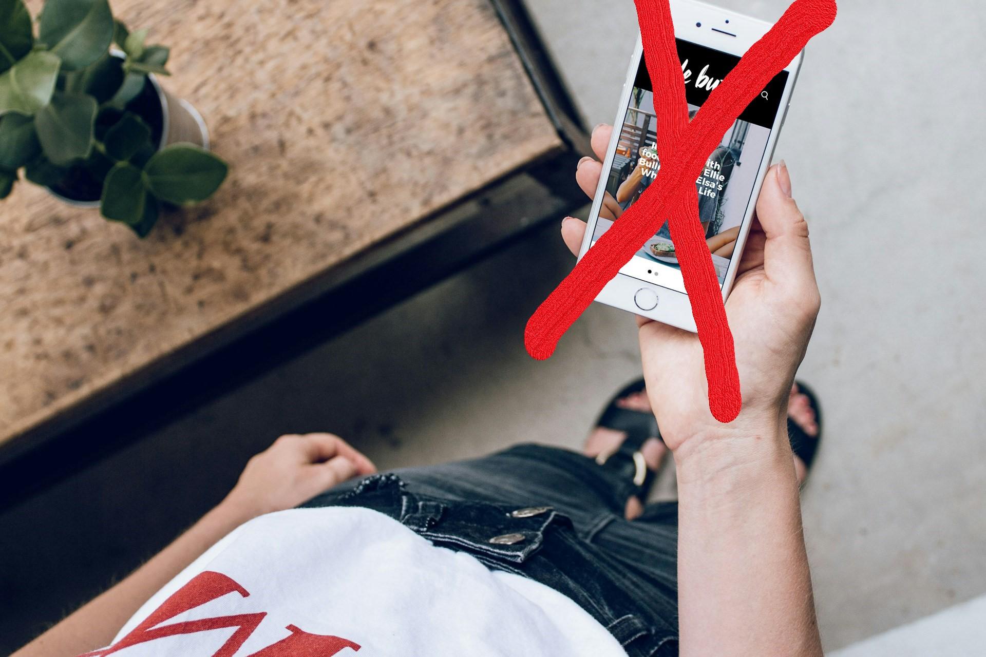 Man sieht von oben eine Hand, die ein Handy festhält, dieses ist mit einem großen roten X durchgestrichen.