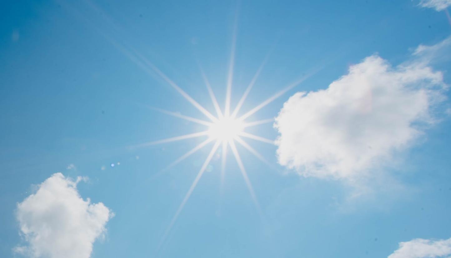 In einem blau-weiß bewölktem Himmel scheint die Sonne und wirft Strahlen wie ein Stern.