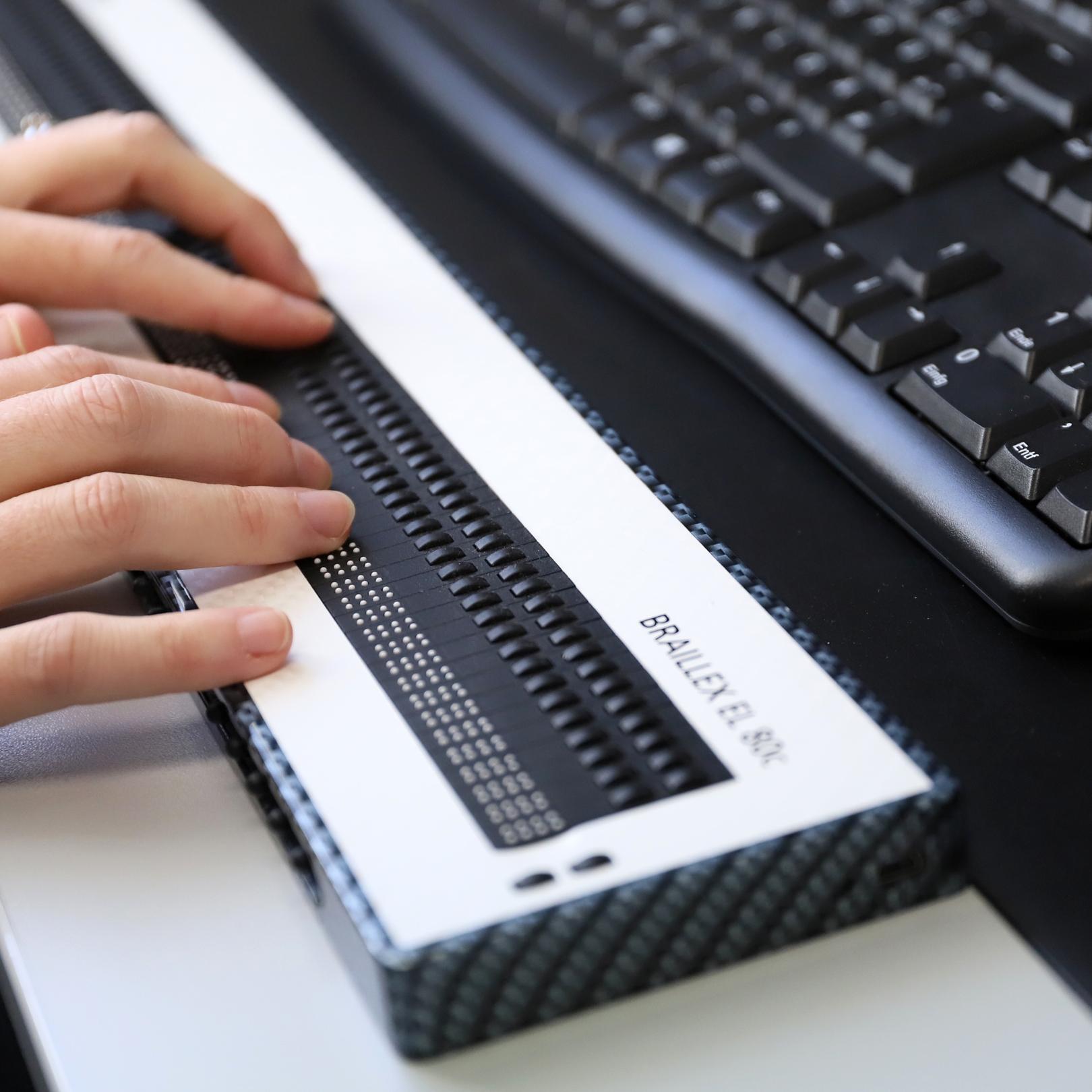 Nahaufnahme einer Braille-Tastatur mit einem paar Hände