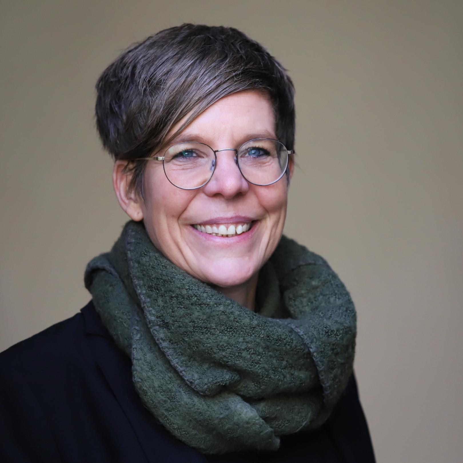 Eine Frau mit kurzen Haaren und Brille lächelt in die Kamera