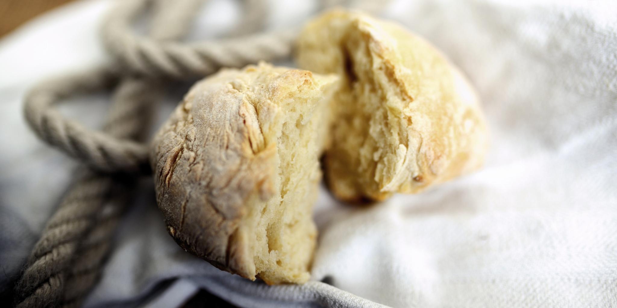 Ein in zwei Teile gebrochenes Brötchen liegt auf einem hellen Tuch, dahinter liegt ein dickes Seil
