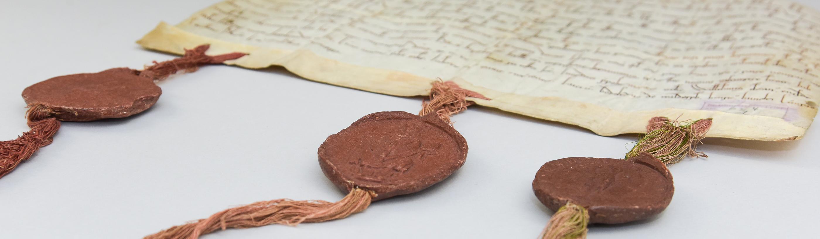 Eine alte Pergament-Handschrift mit drei Bändern am unteren Rand, an denen drei dunkelrote Wachssiegel angebracht sind.