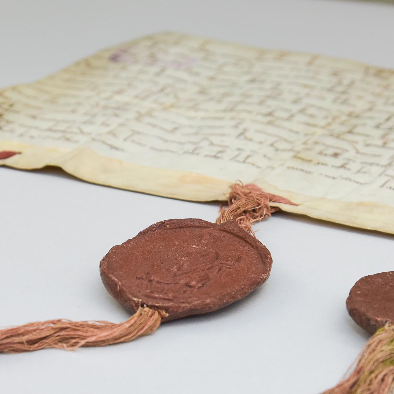Eine alte Pergament-Handschrift mit drei Bändern am unteren Rand, an denen drei dunkelrote Wachssiegel angebracht sind.