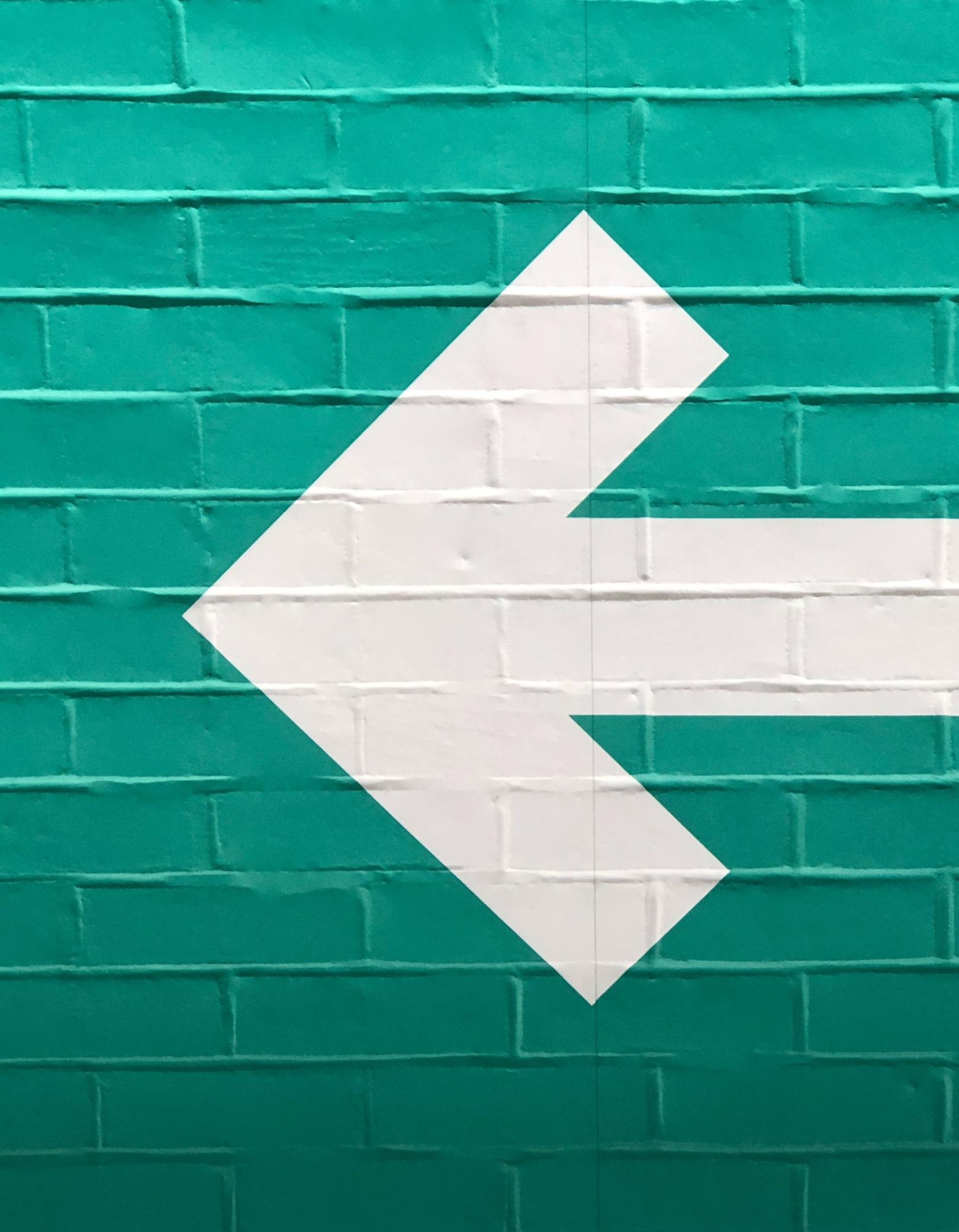 Foto einer grün gestrichenen Wand auf der ein dicker weißer Pfeil nach links zeigt