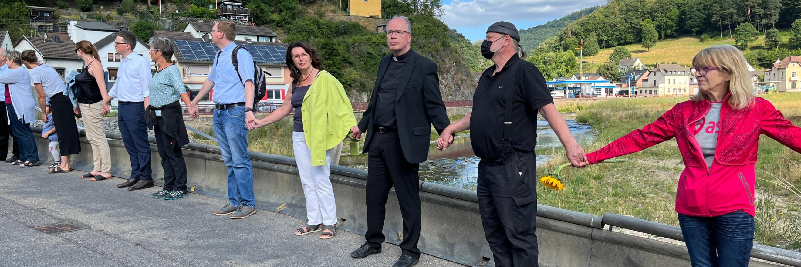 Menschenkette mit Bischof Ackermann und vielen Männern und Frauen auf der Brücke von Ahrbrück zum ersten Jahresgedenken der Flutkatastrophe.