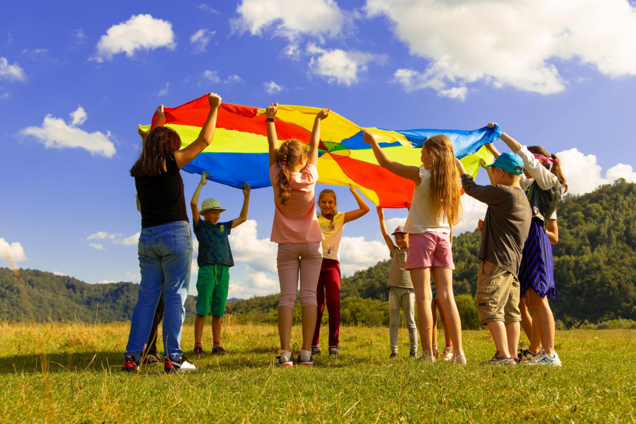 Mehrere Kinder spielen unter einem Schirm in Regenbogenfarben