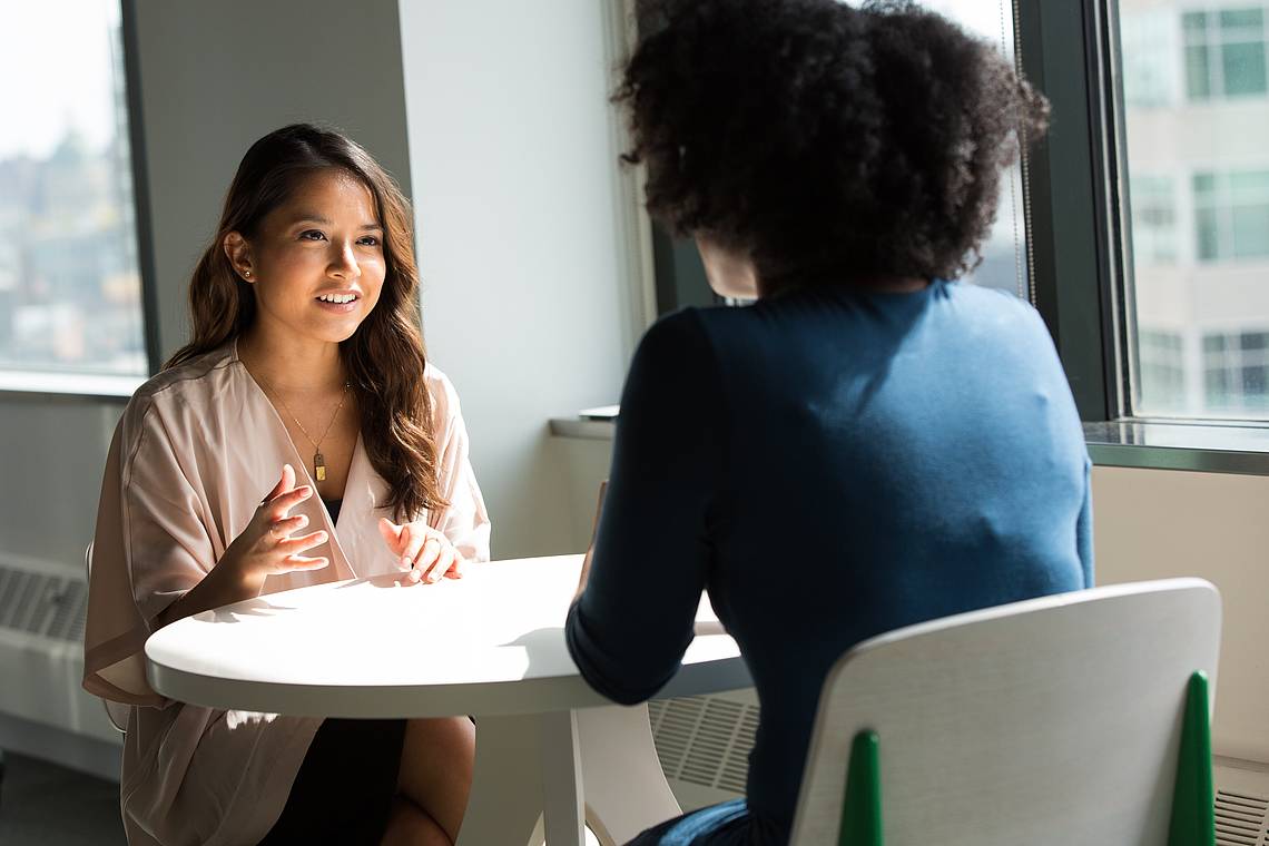 Zwei Frauen sitzen sich gegenüber und reden, die Sonne scheint auf den Tisch