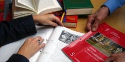 drei Hände auf einem Tisch mit Büchern und Arbeitsmaterialien