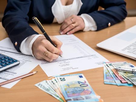 Frau die am Schreibtisch sitzt, Geld zählt und dabei Notizen macht