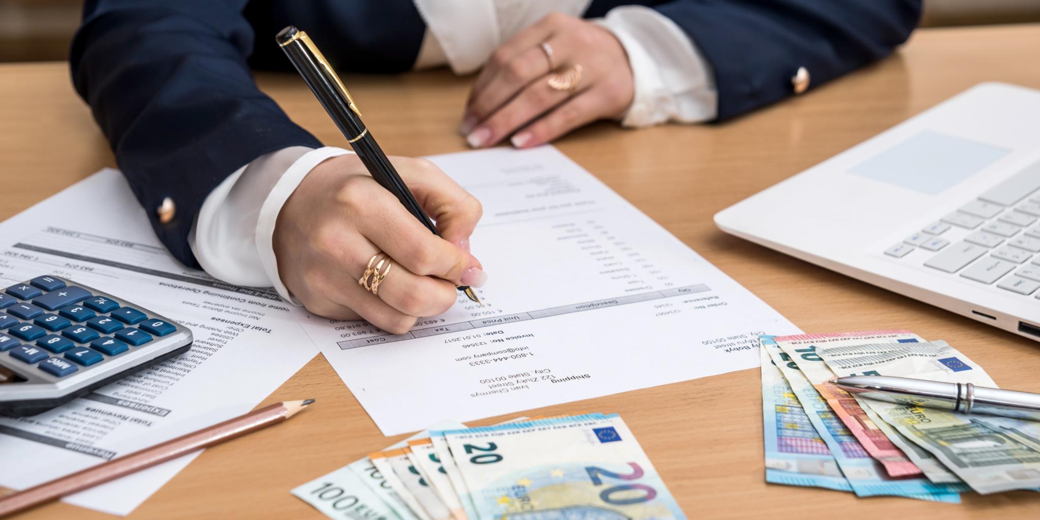 Frau die am Schreibtisch sitzt, Geld zählt und dabei Notizen macht