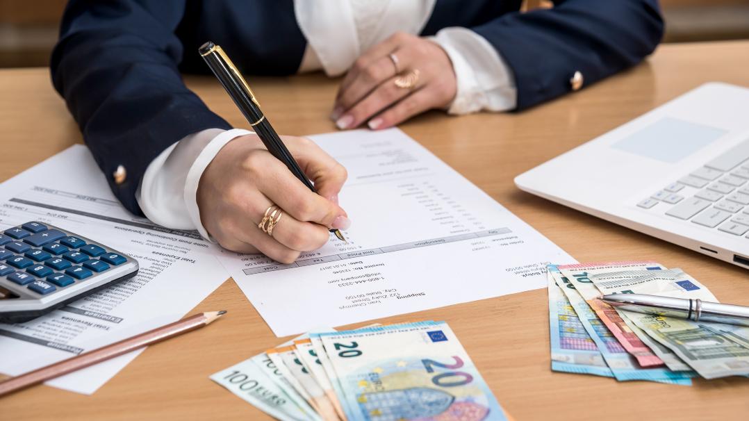 Frau die am Schreibtisch sitzt, Geld zählt und dabei Notizen macht