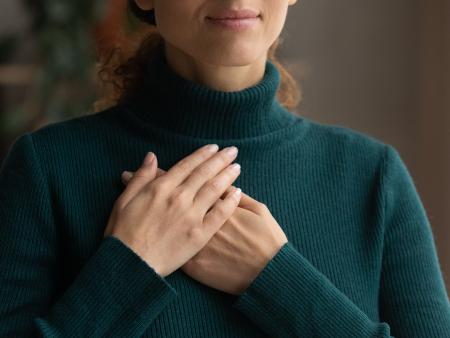 Frau in grünem Rollkragenpullover die beide Hände übereinander auf der Brust liegen hat