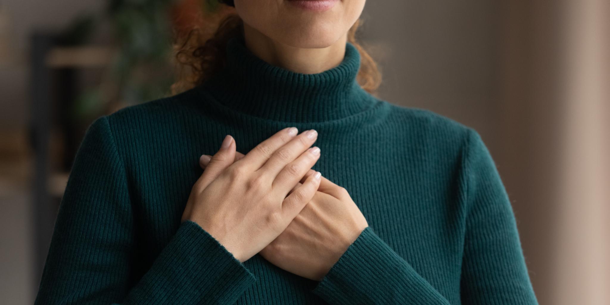Frau in grünem Rollkragenpullover die beide Hände übereinander auf der Brust liegen hat