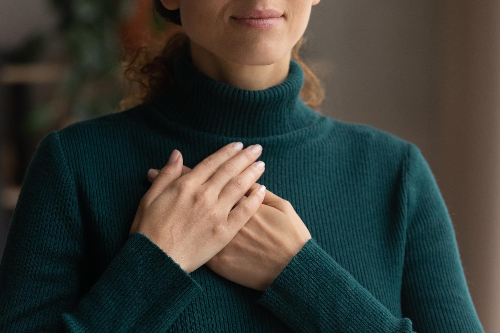 Frau in grünem Rollkragenpullover die beide Hände übereinander auf der Brust liegen hat