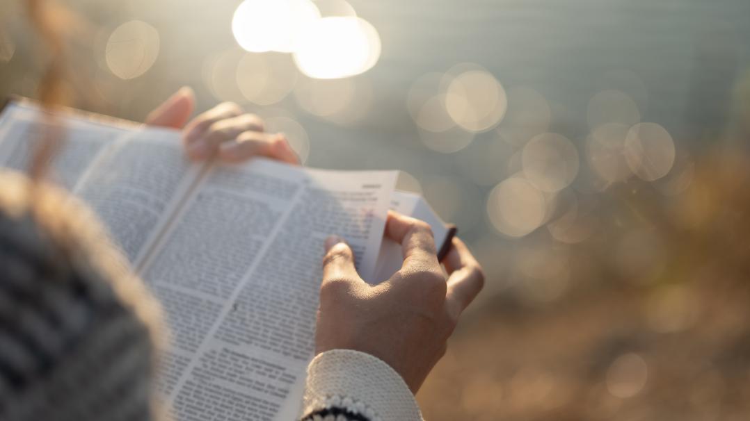 Frau mit Bibel in der Hand vor einem Gewässer