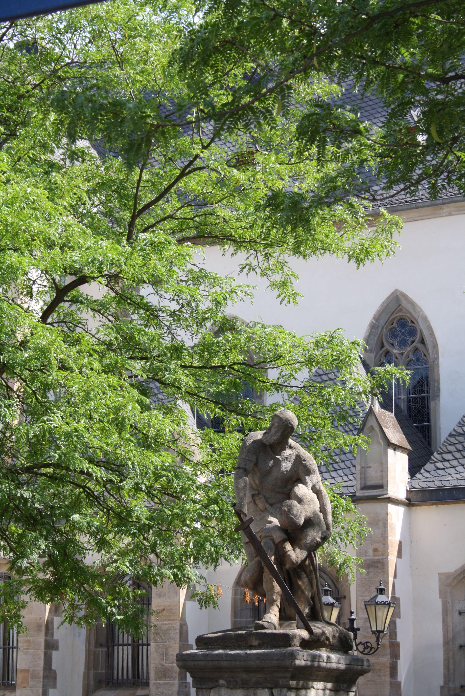 Skulptur und großer Baum vor Kirchengebäude