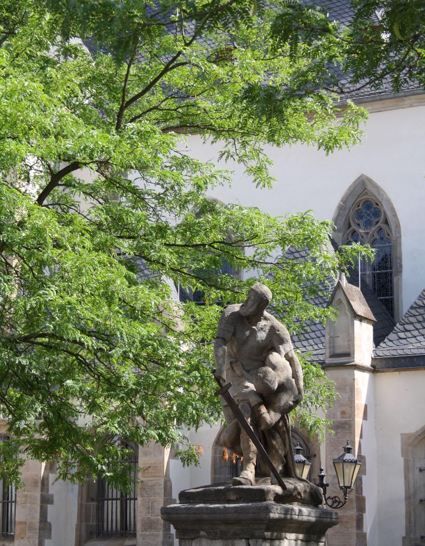 Skulptur und großer Baum vor Kirchengebäude