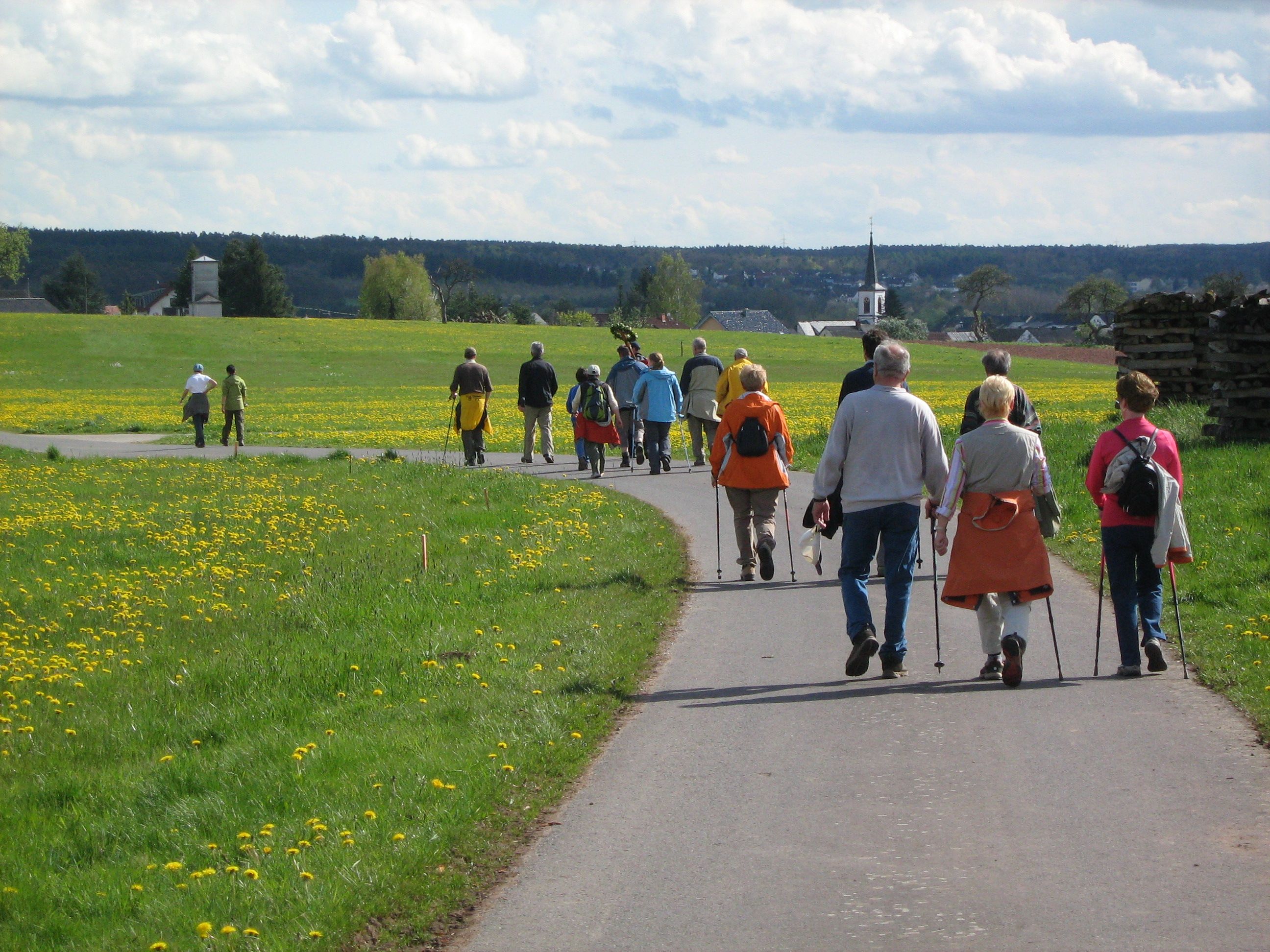 Pilgerer auf gehen auf einem Weg, der durch eine Wiese mit gelben Blumen verläuft.