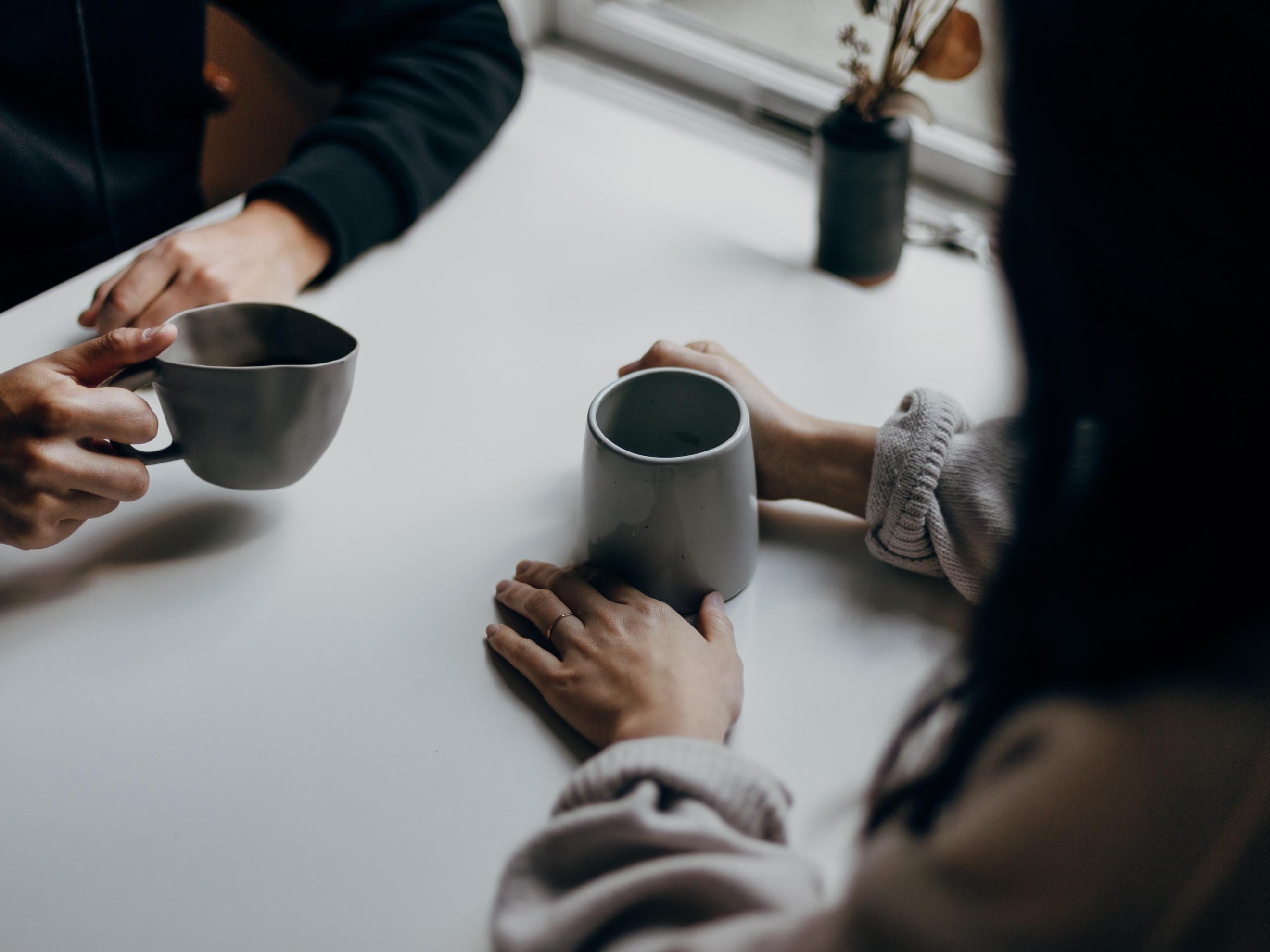 Man sieht zwei Kaffeetassen und die Hände von zwei Menschen, die im Gespräch sind.