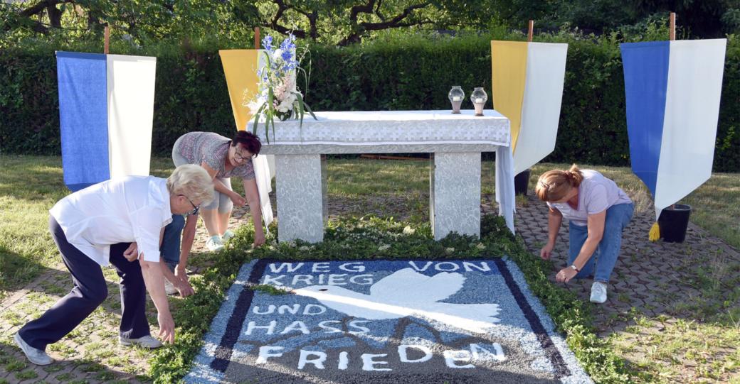 Helferinnen bereiten einen Blumenteppich vor, auf dem 'Weg von Krieg und Hass' und Frieden steht