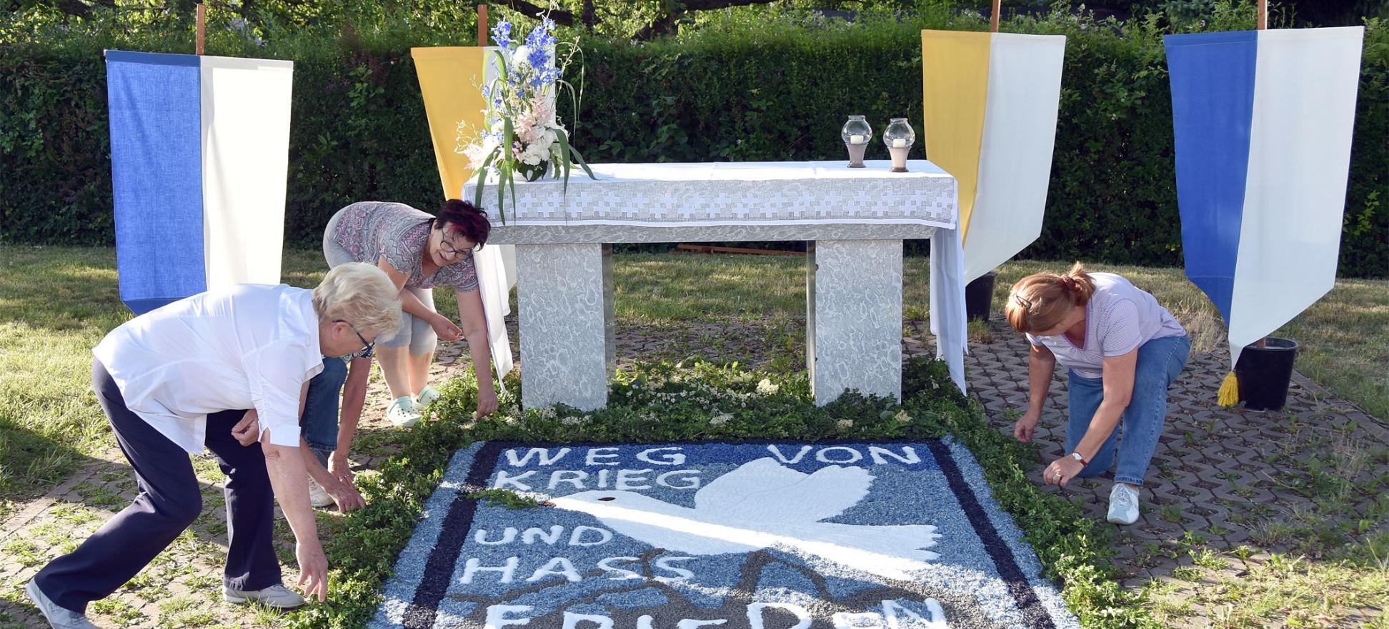 Helferinnen bereiten einen Blumenteppich vor, auf dem 'Weg von Krieg und Hass' und Frieden steht