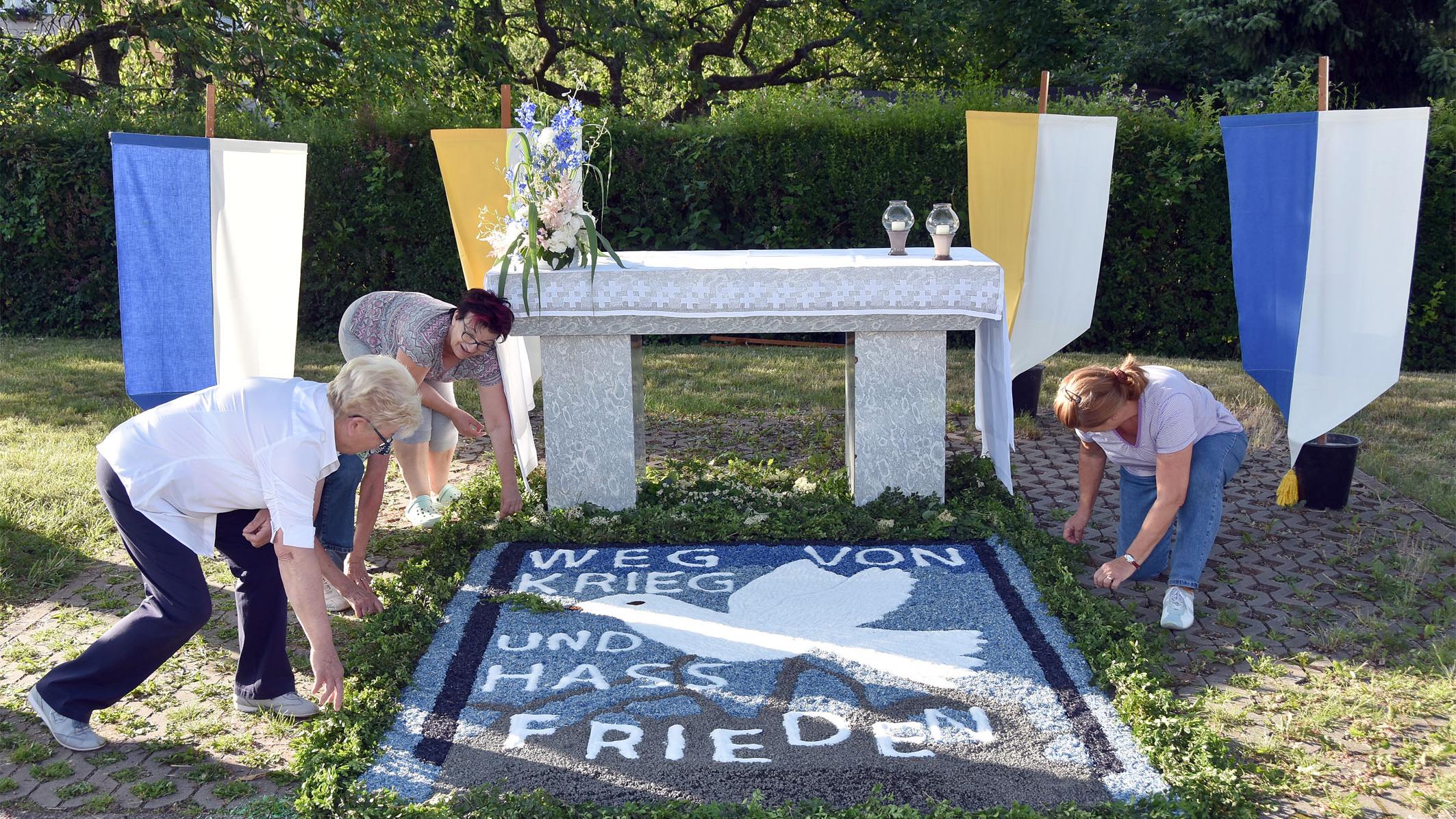 Helferinnen bereiten einen Blumenteppich vor, auf dem 'Weg von Krieg und Hass' und Frieden steht