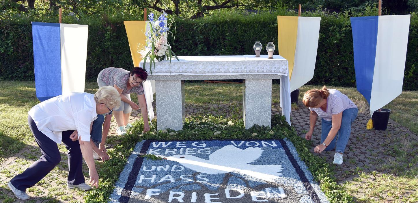 Helferinnen bereiten einen Blumenteppich vor, auf dem 'Weg von Krieg und Hass' und Frieden steht
