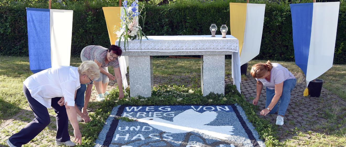 Helferinnen bereiten einen Blumenteppich vor, auf dem 'Weg von Krieg und Hass' und Frieden steht