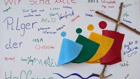 Auf einem Plakat mit der Aufschrift 'Wir sind alle Pilger der Hoffnung' und dem bunten Pilger-Logo haben teilnehmende der Martental-Wallfahrt unterschrieben.
