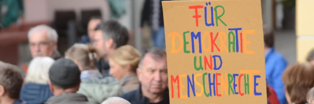 Das BIld zeigt eine Demonstration. Auf einem Plakat steht: Für Demokratie und Menschenrechte.