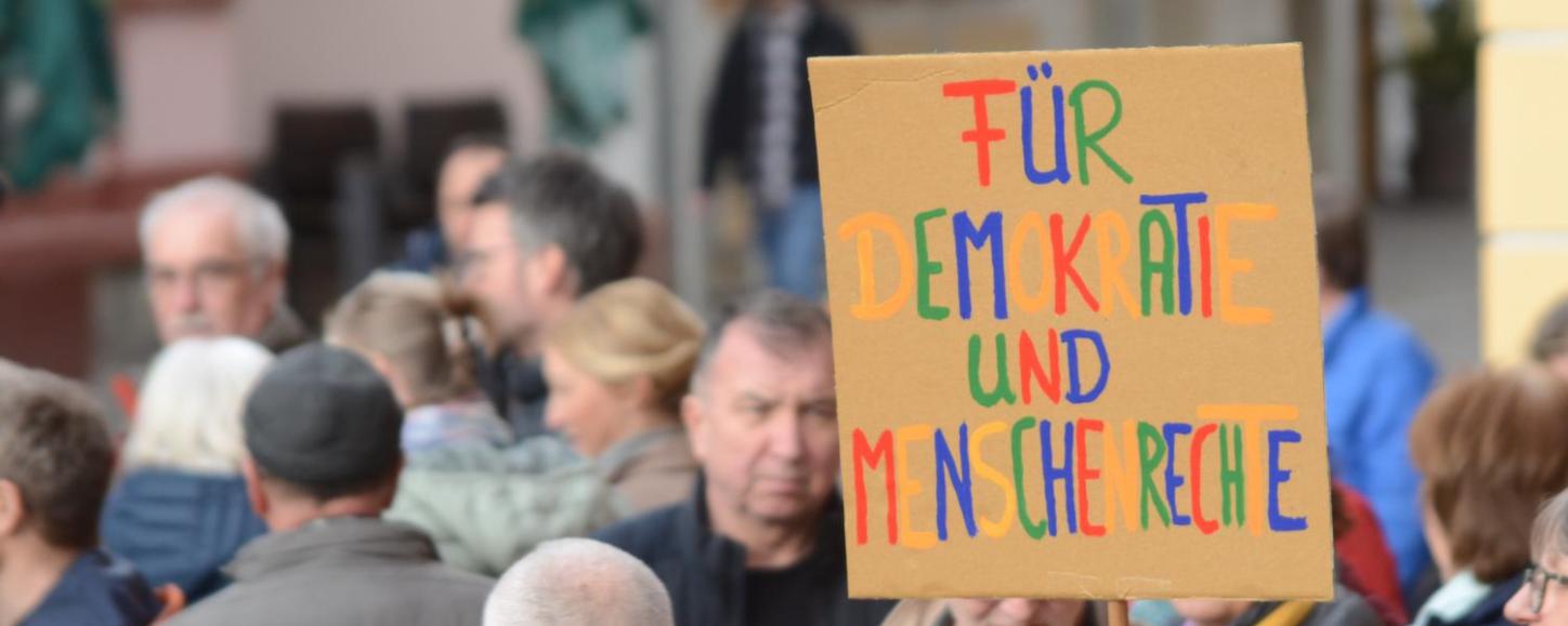 Das BIld zeigt eine Demonstration. Auf einem Plakat steht: Für Demokratie und Menschenrechte.