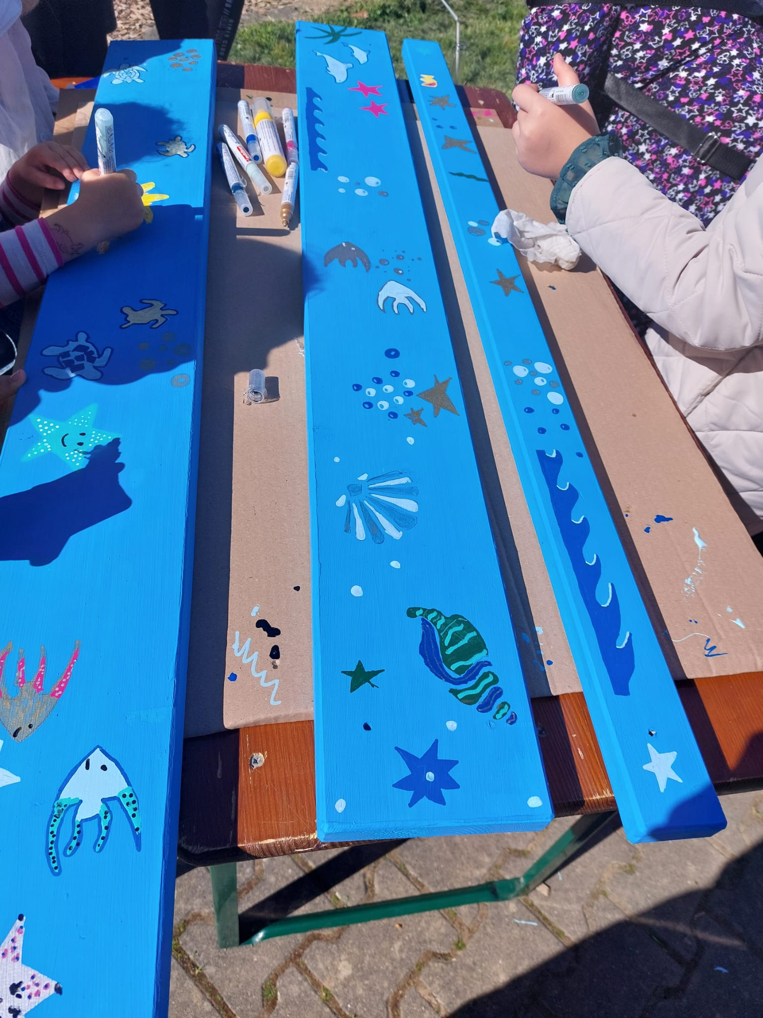 Menschen malen Unterwassermotive auf Holzbretter.