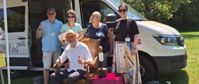 Das Kirchenmobil, ein umgebauter Kleinbus, an einem Veranstaltungsort der Special Olympics. Pastoralreferent Christoph Morgen und weitere 4 Personen stehen davor.