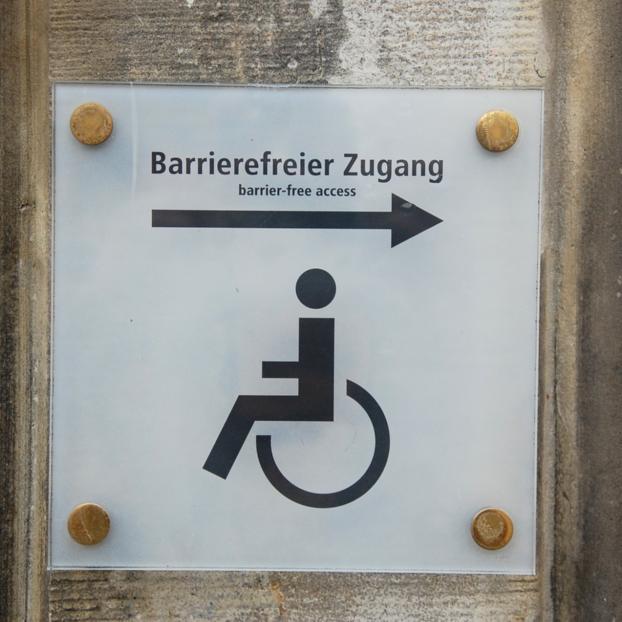 Ein Schild mit einer schwarzen Beschriftung 'Barrierefreier Zugang'. Ein Pfeil zeigt nach rechts, darunter das Piktogramm eines Rollstuhlfahrers.