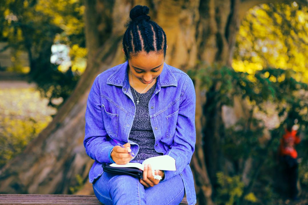 Eine junge Frau sitzt draußen auf einer Bank und liest in einem Buch.