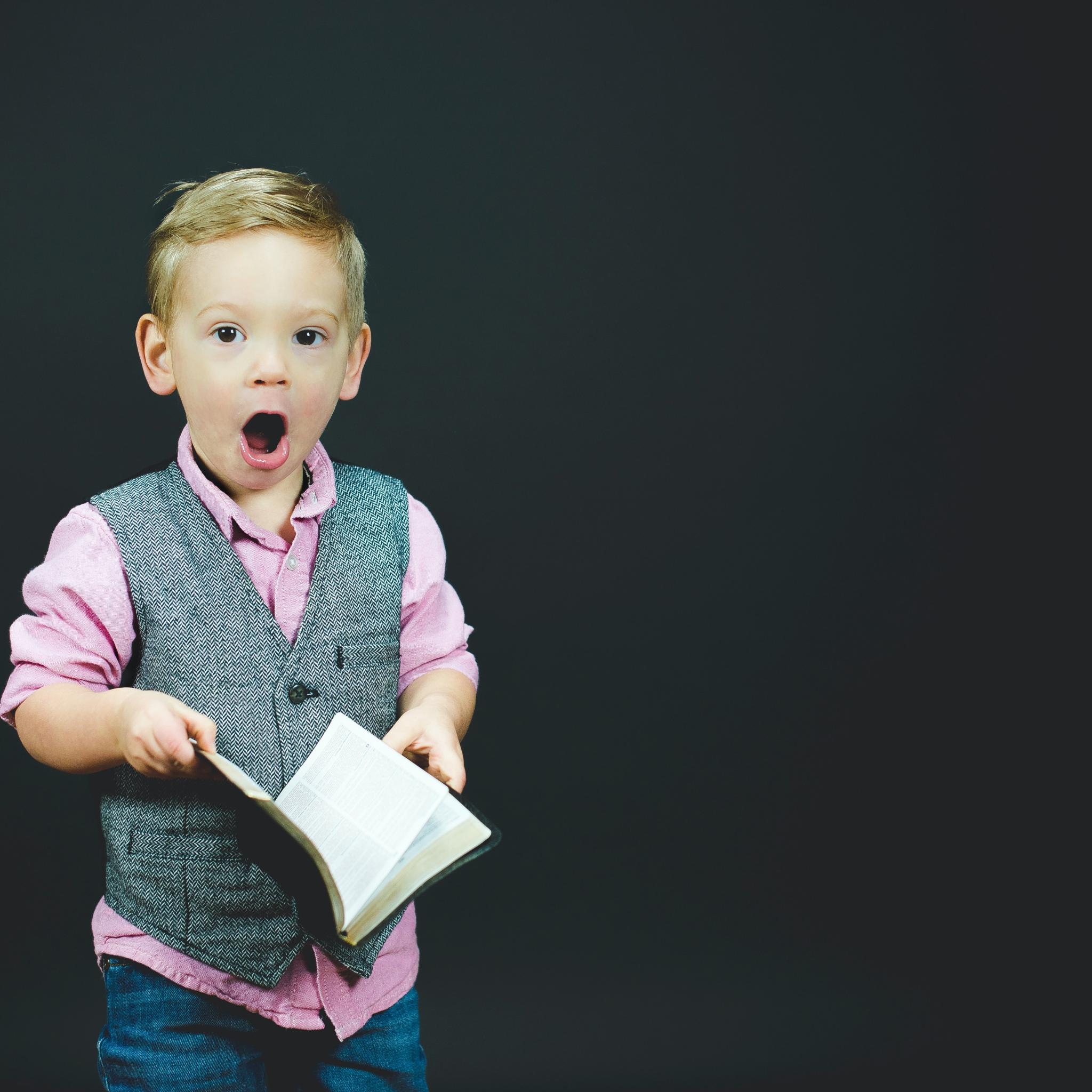 Man sieht einen kleinen Jungen, der ein Liederbuch in der Hand und den Mund zum Singen geöffnet hat