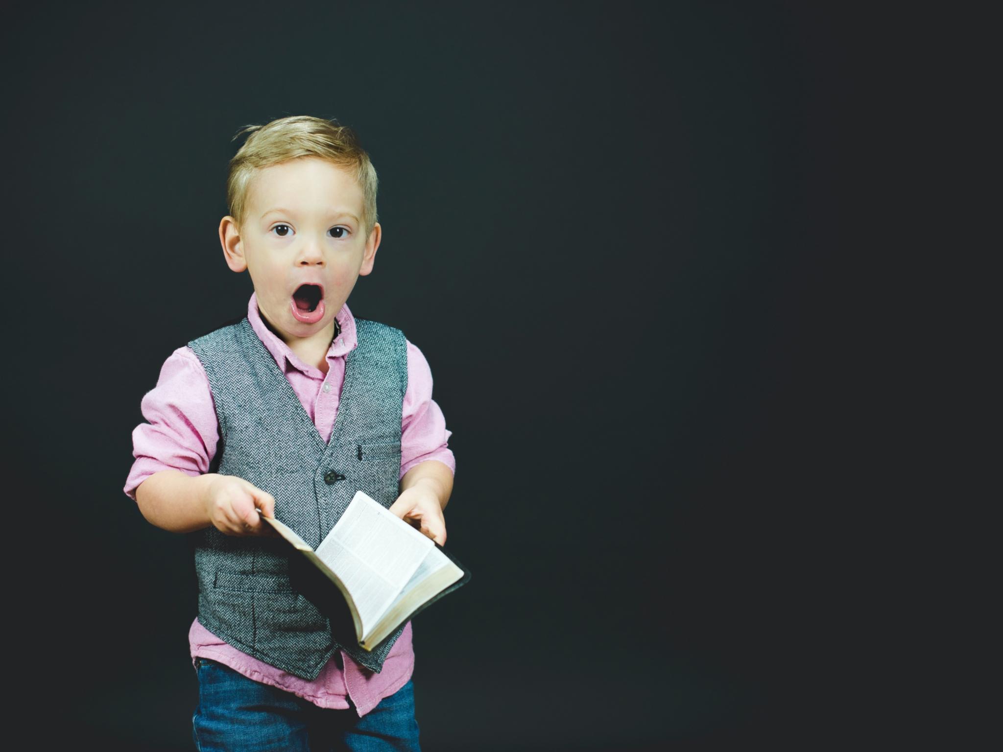 Man sieht einen kleinen Jungen, der ein Liederbuch in der Hand und den Mund zum Singen geöffnet hat