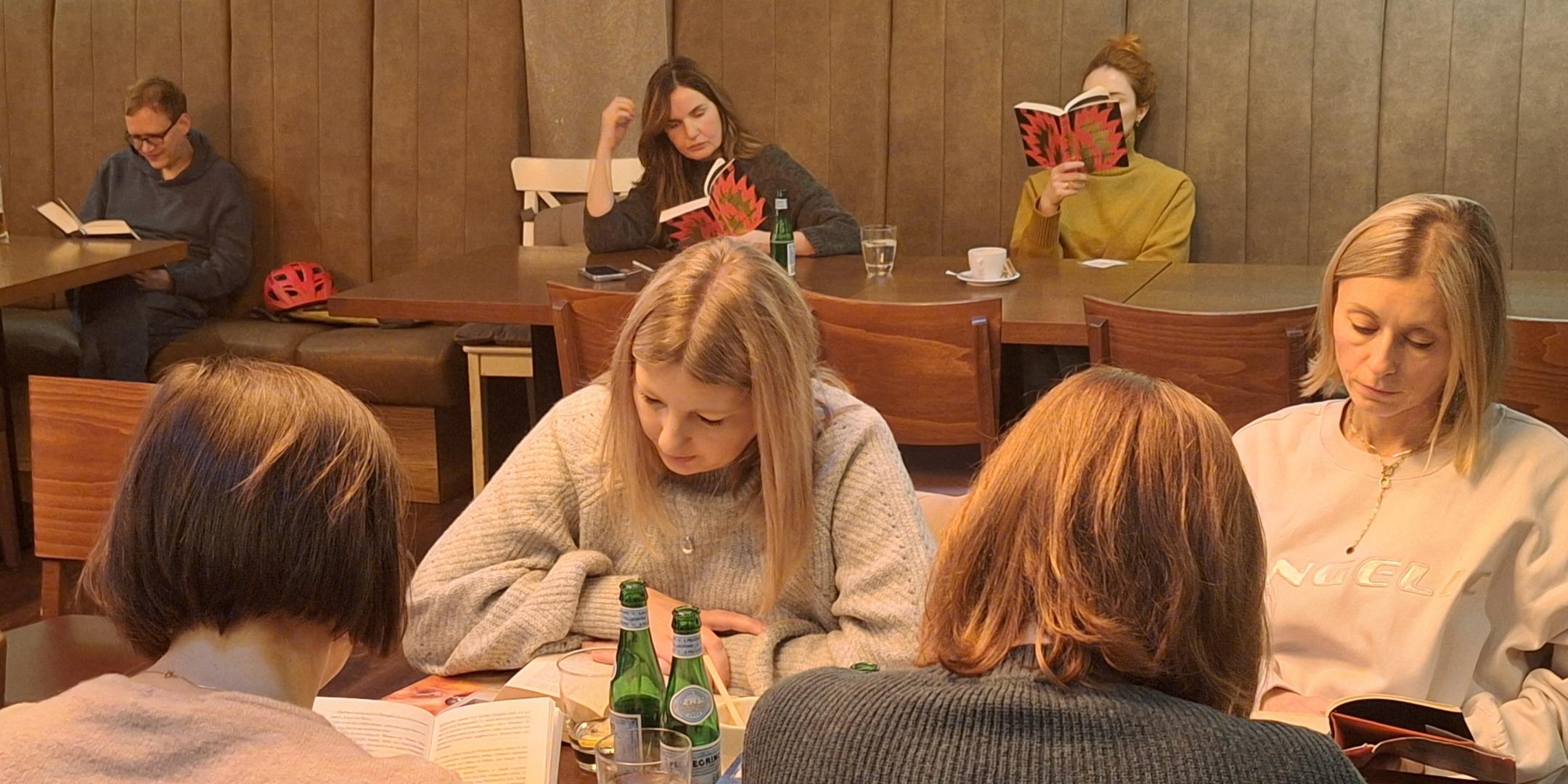 mehrere junge Menschen sitzen an einem Tisch und lesen Bücher