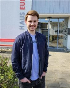 Ein junger Mann mit sportlicher Jacke und T-Shirt lächelt in die Kamera