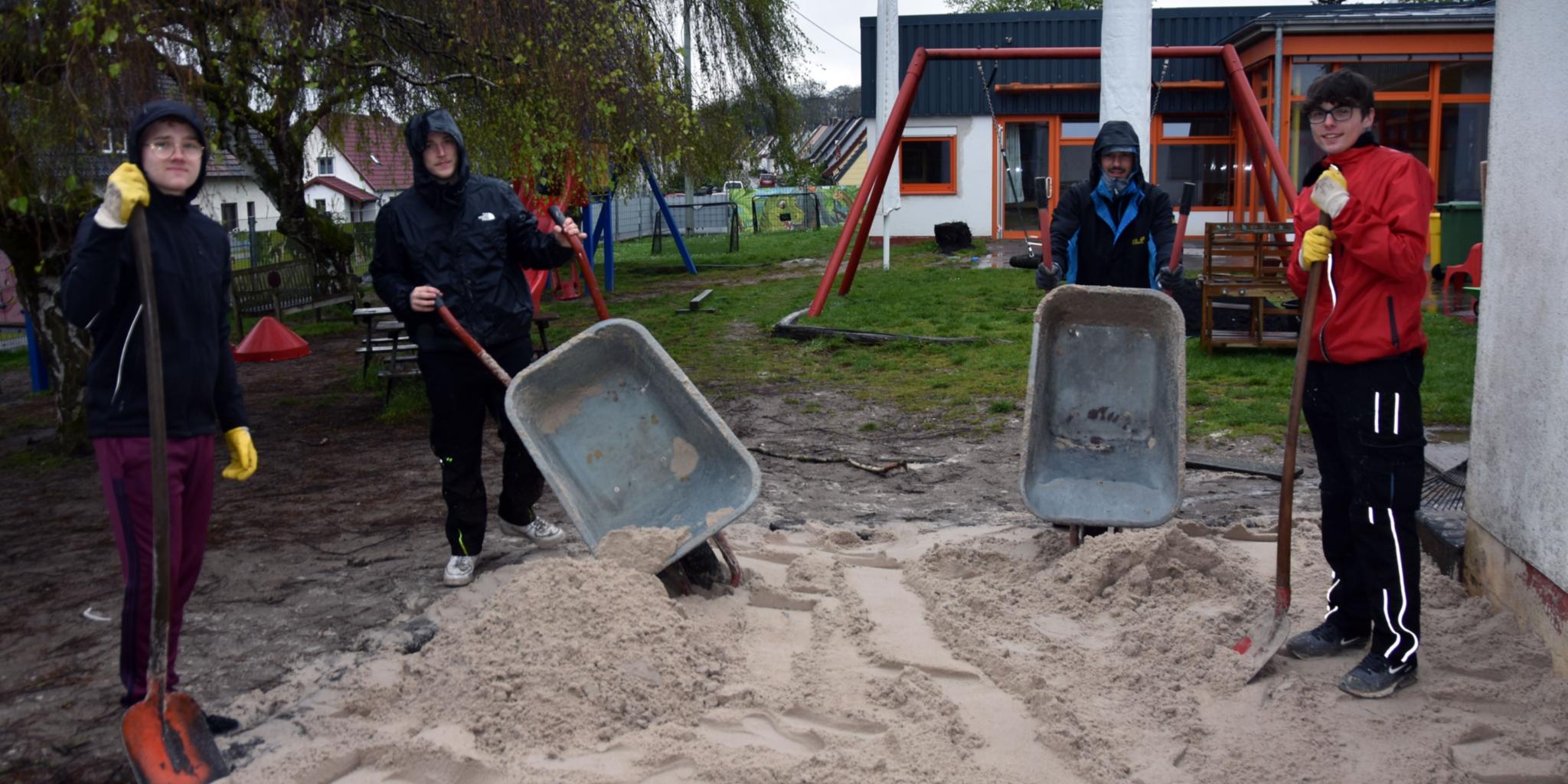 Mit Schubkarren und Schaufeln befüllen Justin, Valentin, Luca und Yannik (vlnr) den Sandkasten der Kita St. Josef mit gespendetem Sand.