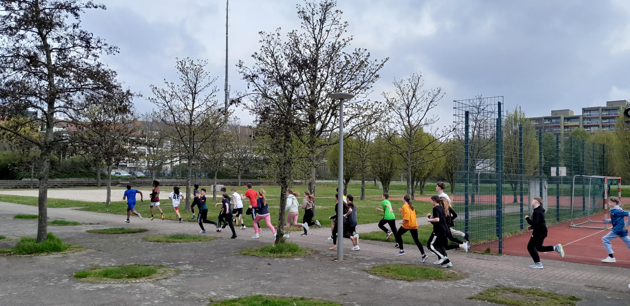 Kinder in Sportkleidung beim Joggen, vorbei an einem Sportgelände
