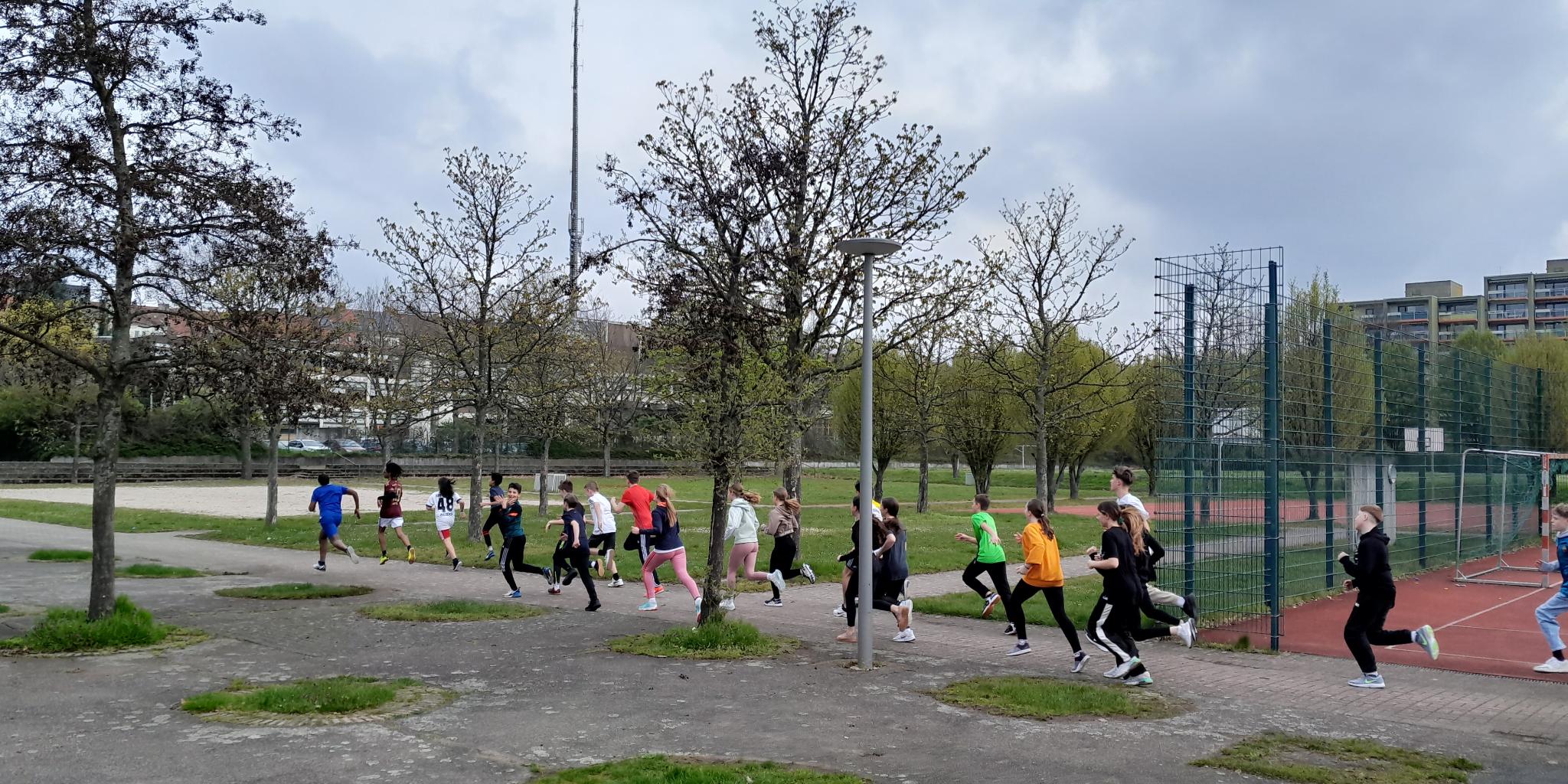 Kinder in Sportkleidung beim Joggen, vorbei an einem Sportgelände